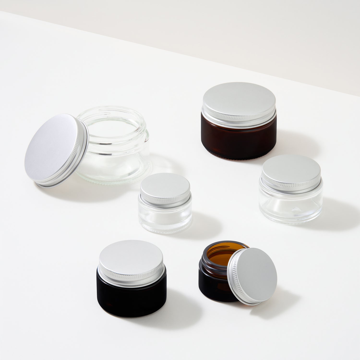 Collection of glass cosmetic screw lid jars on white background.